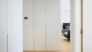 Quarto moderno e minimalista com um guarda-roupa branco, televisão de tela plana e piso de madeira.