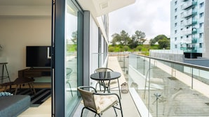 Uma sala de estar moderna com uma televisão grande, assentos confortáveis e uma varanda de vidro com vista para a cidade.