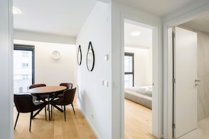 A modern room with a wooden dining table and chairs, a bed with a striped blanket, and a white door. - Modern Lisbon Balcony AND Pool by Homing (Lisbon)