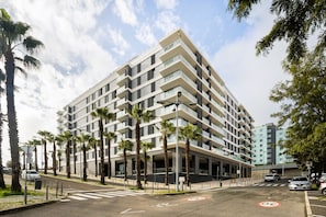 A modern multi-story building with a flat facade, surrounded by palm trees and a clear sky. - Modern Lisbon Balcony AND Pool by Homing (Lisbon)