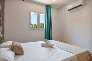 A hotel room with a bed, a window, a curtain, and an air conditioning unit. - Dream Villa with Private Pool in Cala Romántica (S'Estany d'en Mas) (Romàntica)