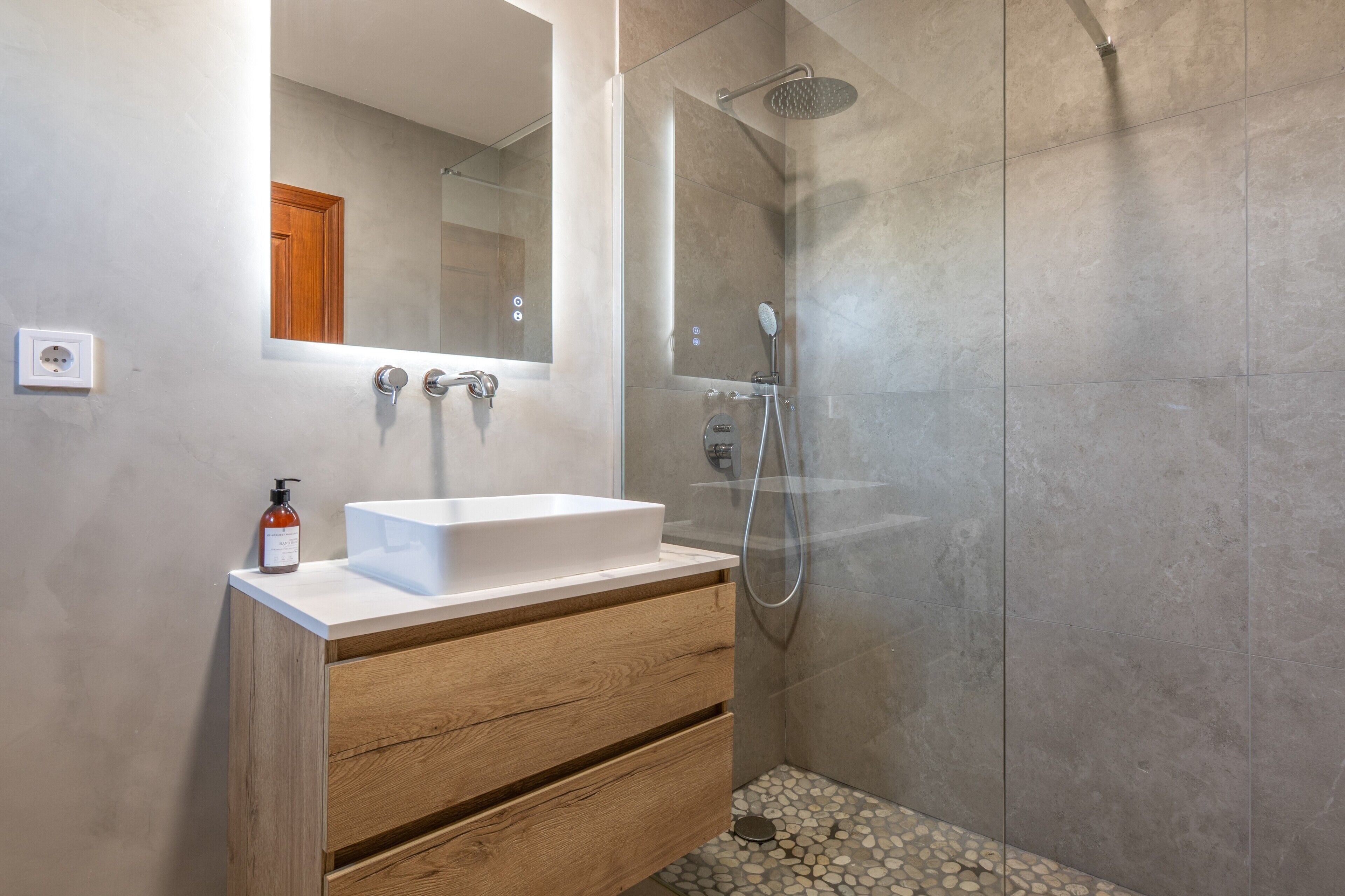 Une salle de bain moderne avec un lavabo blanc, un meuble-lavabo en bois et une douche séparée par des parois en verre.