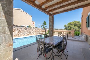 Eine Terrasse im Freien mit Pool, Steinmauern und einem Tisch mit Stühlen.
