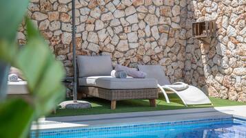 A stone wall, a wicker lounge chair, and a pool.