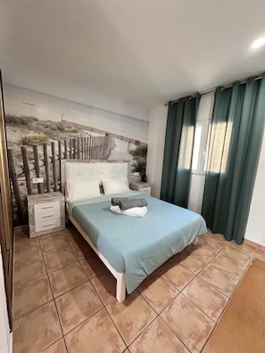 A bedroom with a bed, a nightstand, a wall mural, and a window with curtains.