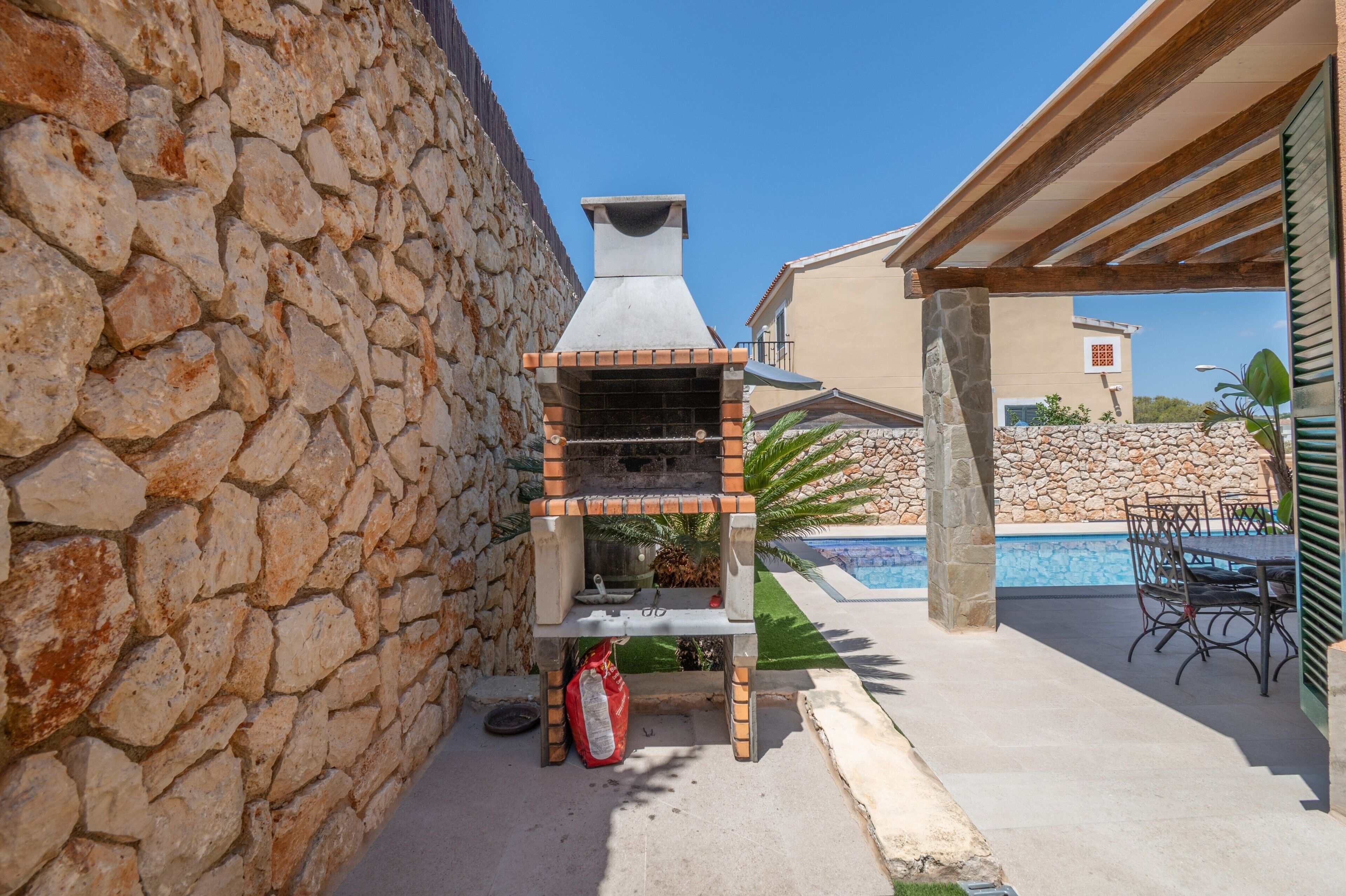 Un muro de piedra, una parrilla, una piscina y mobiliario de exterior.