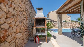 Un muro de piedra, una parrilla, una piscina y mobiliario de exterior.