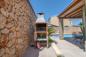 Un muro de piedra, una parrilla, una piscina y mobiliario de exterior.