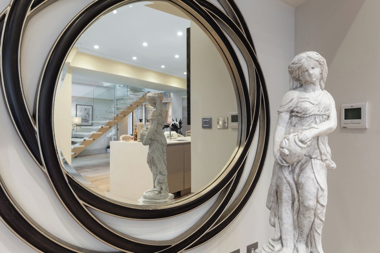A marble statue in a modern interior space with a large mirror reflecting a staircase and a reception area.