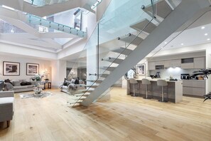 Een ruime woonkamer met een moderne trap, een keuken met barstoelen en een gezellige zithoek met een bank en decoratieve kussens.