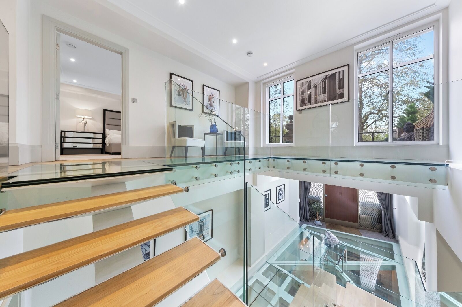 A modern interior with a glass staircase connecting two floors, wooden railings, and artwork on the walls.