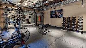 Een sportschool met fitnessapparatuur, een ventilator en een wandrek met haltergewichten.