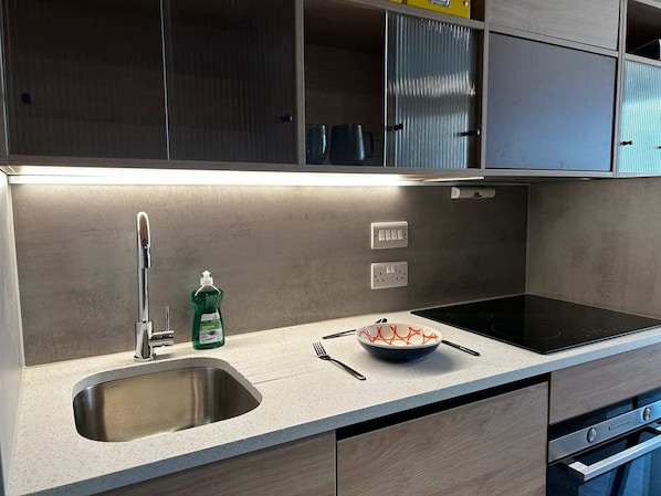 Una cucina moderna con un lavello in acciaio inox, una bottiglia di detersivo per piatti, una ciotola con bacchette e un piano cottura a induzione.