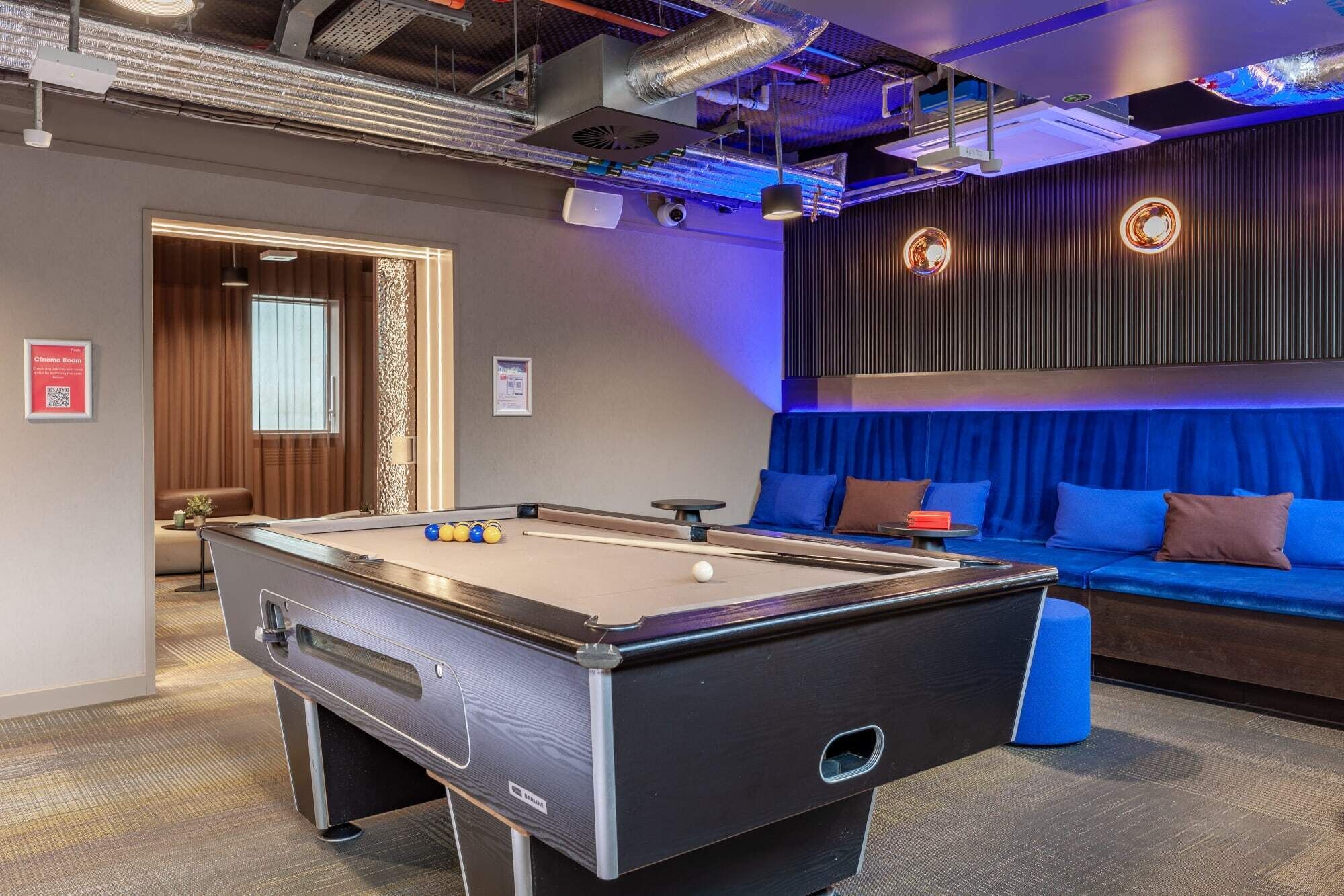 A pool table in a room with a blue sofa and a cinema room sign.
