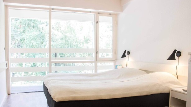 A modern bedroom with a large bed, wooden flooring, and a view of greenery through a sliding door. - 2 Rooms, 3+2 People, 38m2 (Nexø)