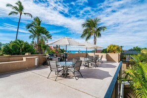 Eine Terrasse im Freien mit Tischen, Stühlen, einem Grill und Palmen.