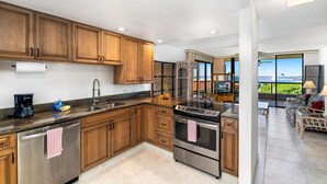 A modern kitchen with wooden cabinets, stainless steel appliances, and a large island. - Kona Pacific E734: Penthouse Corner unit, Best Ocean Views, AC, Walk to town (Kailua Kona)