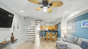 A living room with a sofa, a dining area with chairs, a kitchen in the background, and a staircase. - Beautiful, Pet Friendly, Waterfront Townhome at San De Luna #3! (Pensacola Beach)