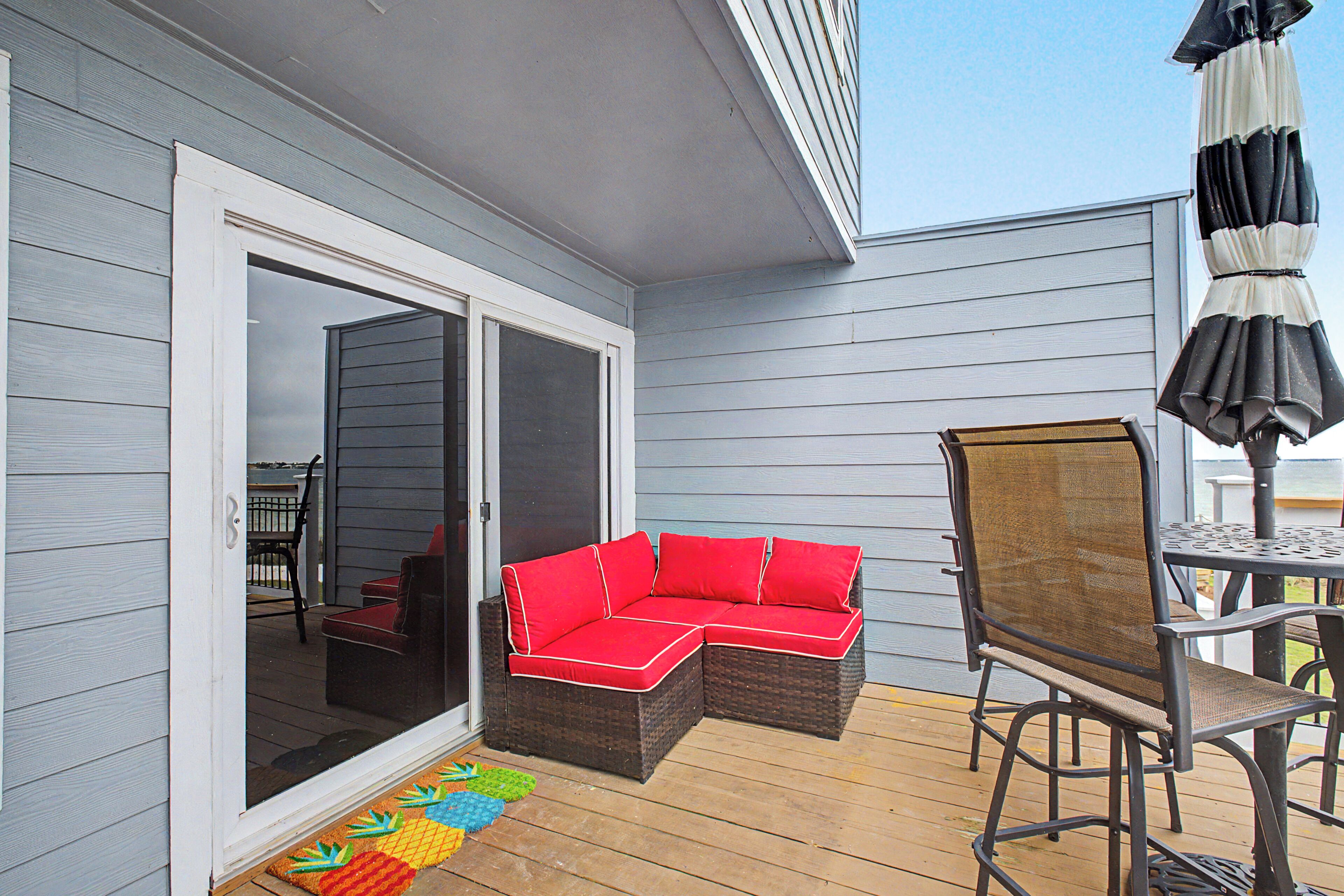 A covered patio with a sliding glass door, a red sectional sofa, a metal table with chairs, and an umbrella.