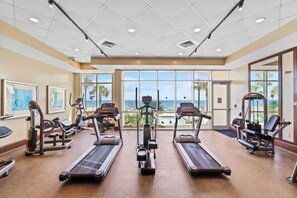Un gimnasio con cintas de correr, elípticas y máquinas de pesas, con grandes ventanales y vistas a la playa.