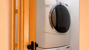 Een kleine wasruimte met een wasmachine en droger in een dubbele unit, een houten deur en een betegelde vloer.