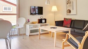 Una sala moderna con una televisión de pantalla plana, un sofá, una mesa de centro y un comedor con sillas.
