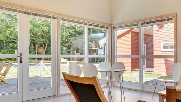 Una habitación con grandes puertas de vidrio correderas, una silla de madera, una pequeña mesa redonda y vista a un edificio rojo en el exterior.