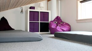 Una habitación con techo inclinado, un armario blanco con cajas de almacenamiento moradas y un sillón informal morado, además de un sofá gris.