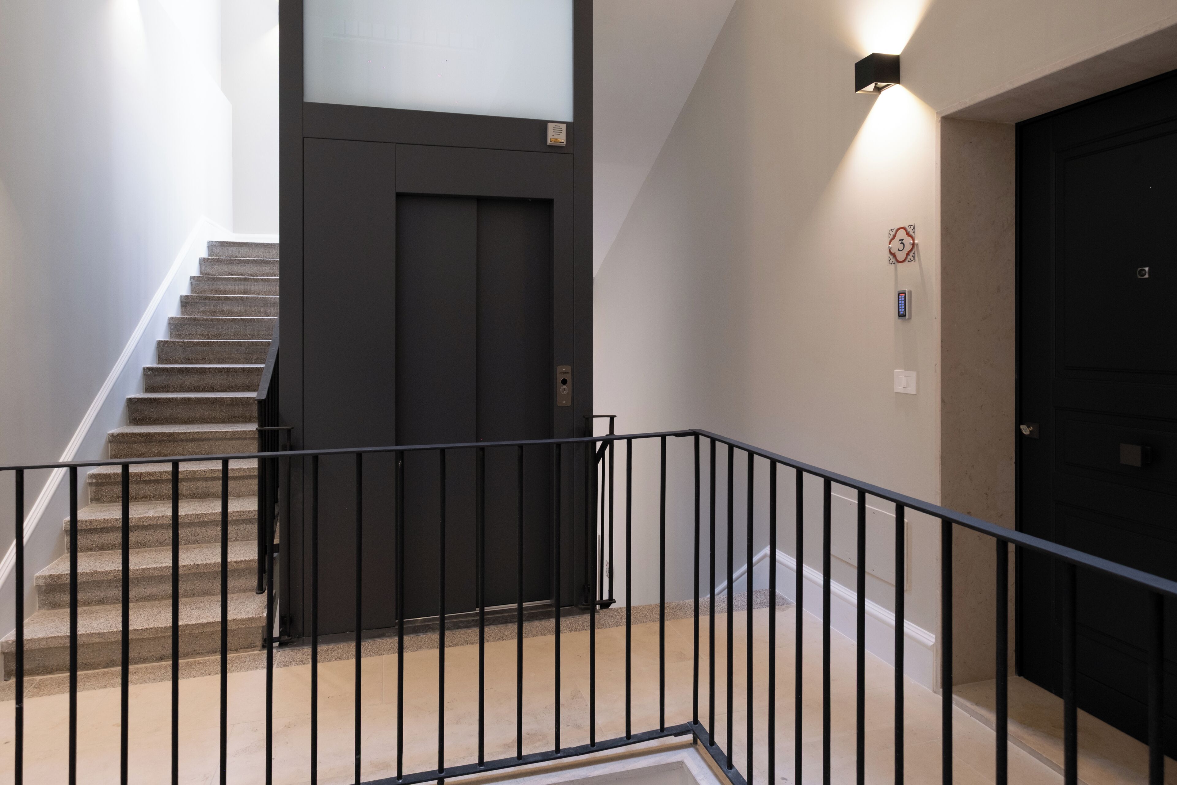 Un escalier avec une rampe noire menant à une porte sombre.