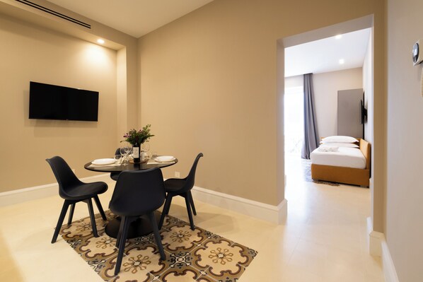 Une chambre d’hôtel dotée d’un coin repas comprenant une table et des chaises, d’un téléviseur à écran plat fixé au mur et d’un lit avec une tête de lit.