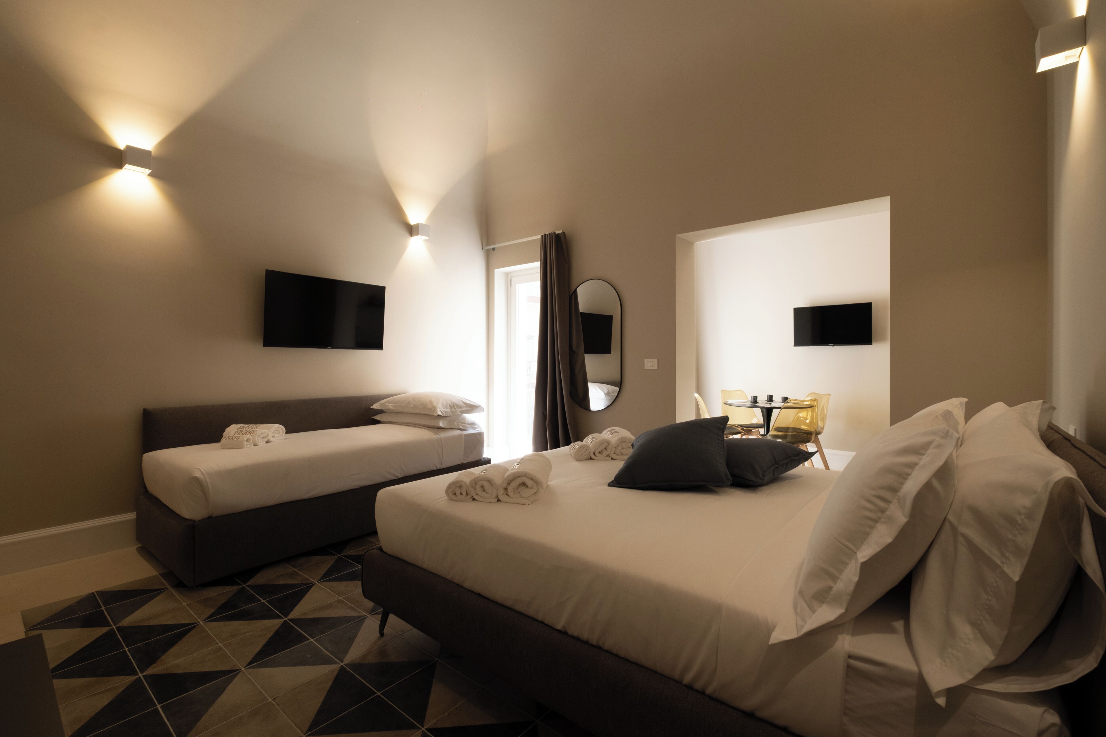 Ein Hotelzimmer mit zwei Betten, einem großen Spiegel und einem an der Wand befestigten Flachbildfernseher.