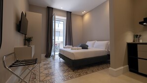 Ett modernt hotellrum med en säng, ett skrivbord, en stol, en TV och en balkong med gardiner.