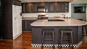 Una cocina moderna con armarios de madera oscura, estufa de acero inoxidable, microondas e una isla grande con taburetes de bar.