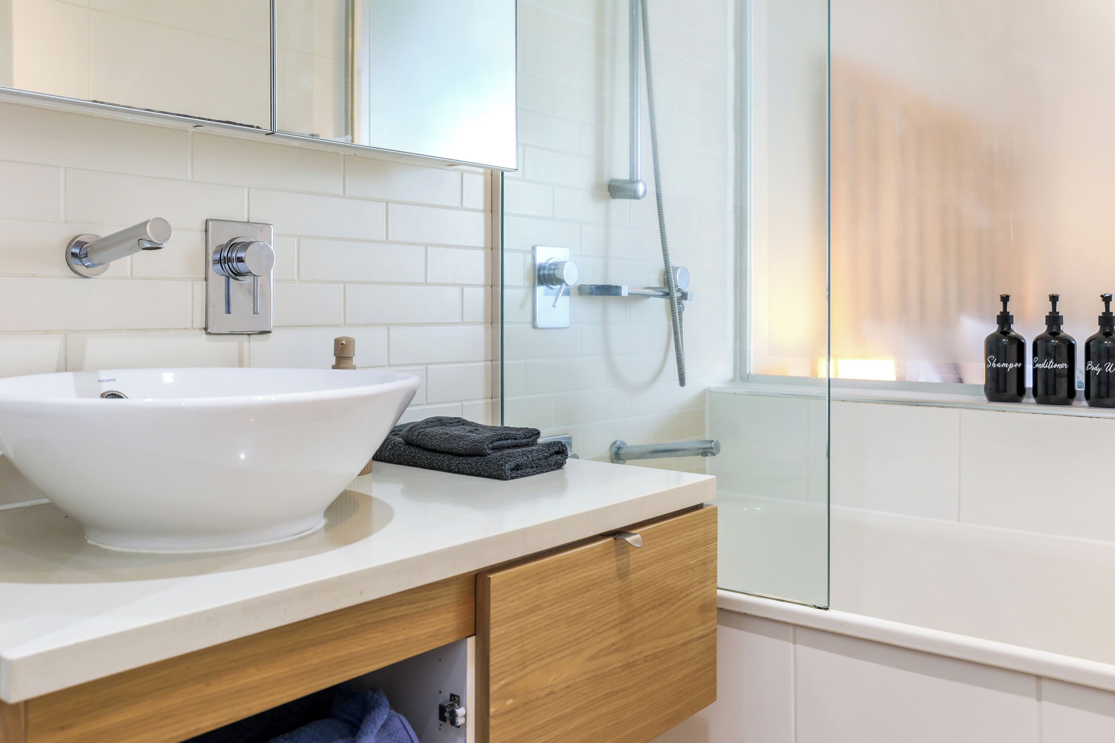 A modern bathroom with a large white sink, a glass shower enclosure, and a vanity with a mirror.
