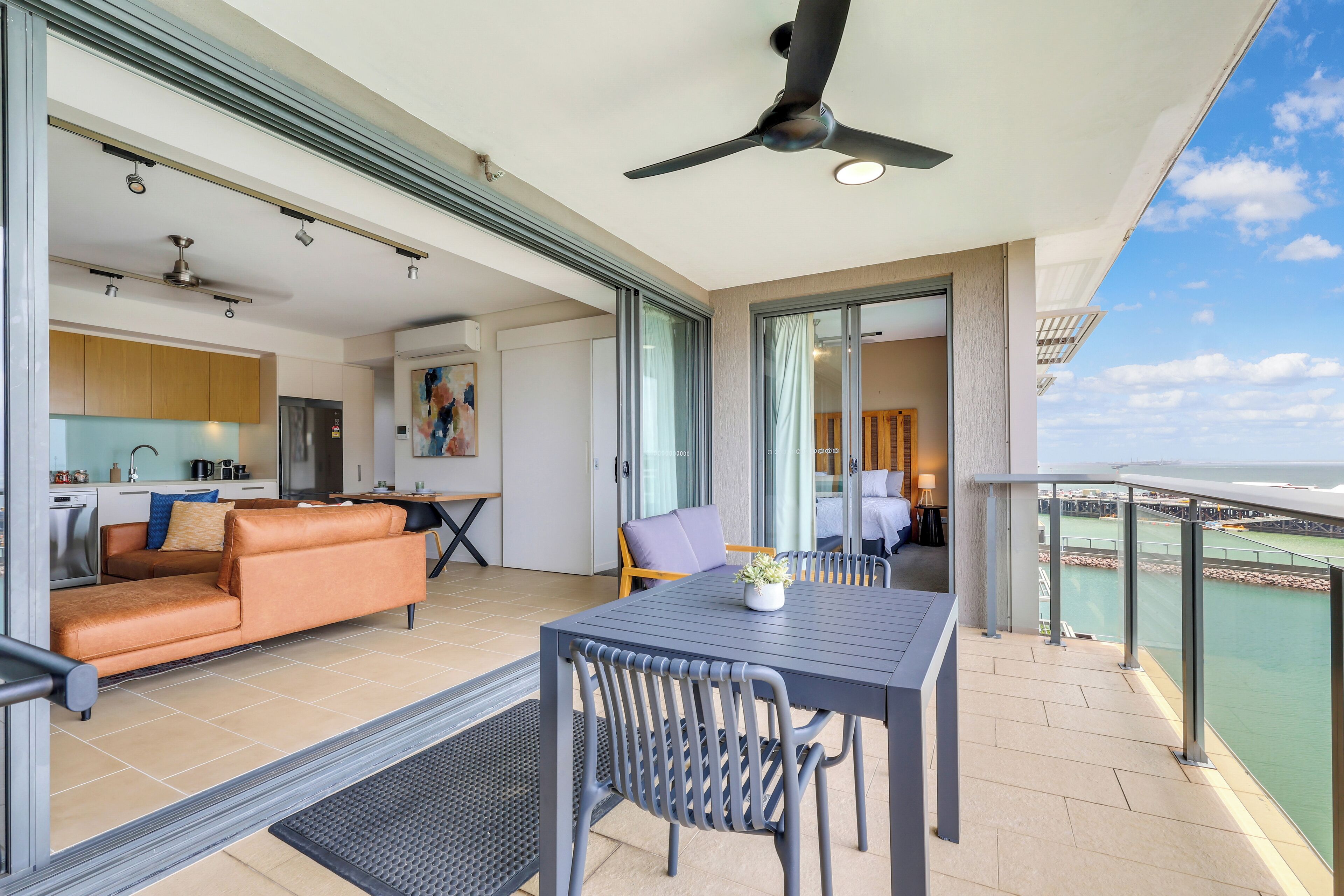 Un espacio habitable moderno con sofá, mesa de comedor y sillas, un balcón con vista al mar, y una cocina al fondo.