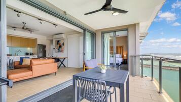 Un espacio habitable moderno con sofá, mesa de comedor y sillas, un balcón con vista al mar, y una cocina al fondo.