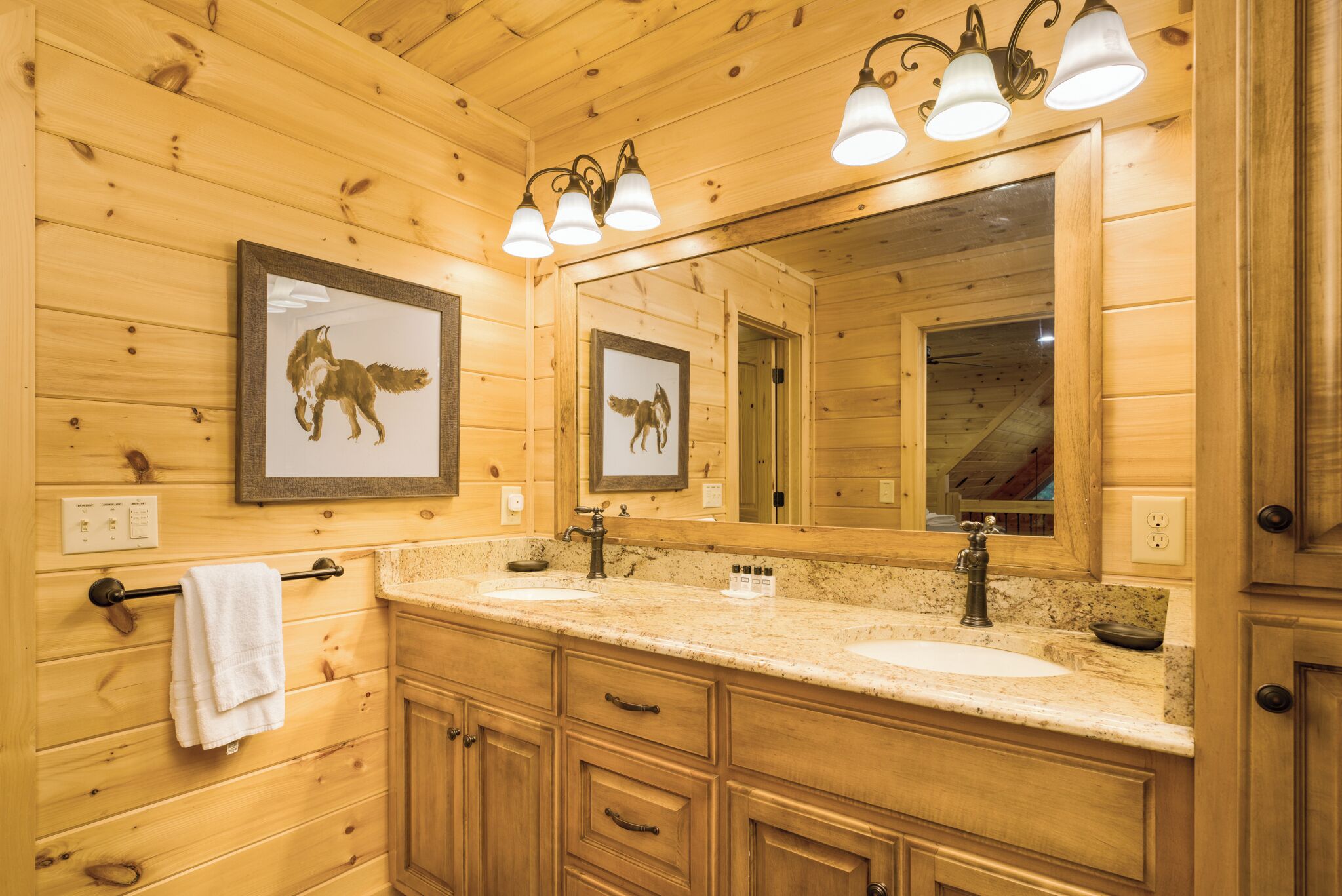 Une salle de bain rustique, avec des murs en bois, un grand miroir, deux lavabos et des photos de loups encadrées.