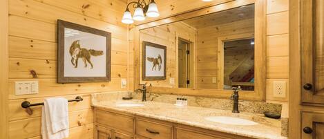Une salle de bain rustique, avec des murs en bois, un grand miroir, deux lavabos et des photos de loups encadrées.
