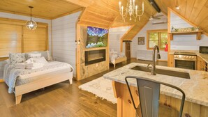 Un dormitorio acogedor en el ático con una cama, chimenea y una zona de cocina con fregadero y estufa.