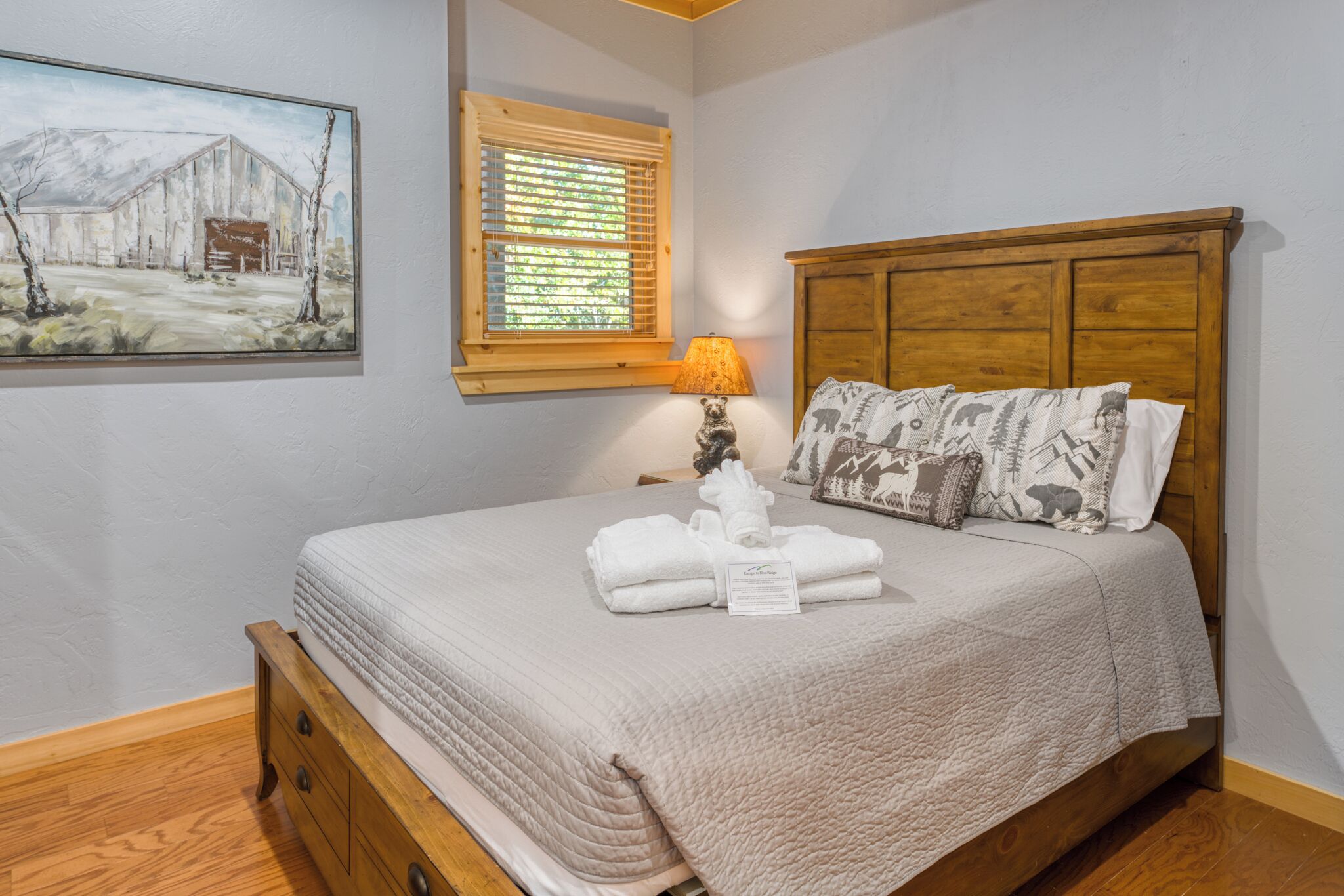 Une chambre avec un lit en bois, une table de chevet avec une lampe, un tableau au mur et une fenêtre avec des stores.