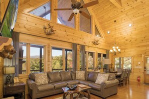 Ein geräumiges Wohnzimmer mit einer großen Ledersofa, Holzbalkendecke und großen Fenstern mit Blick ins Freie.