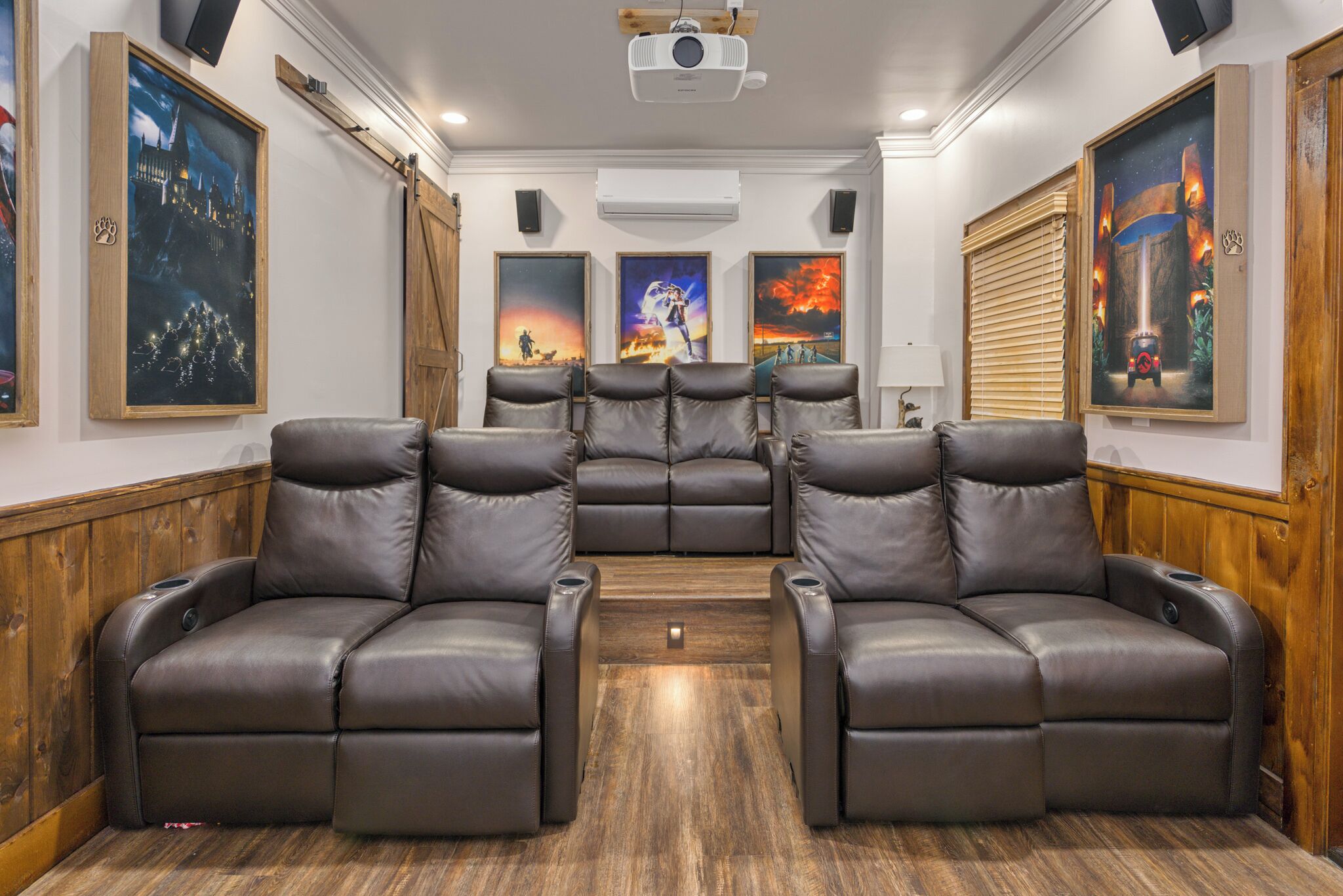 A home theater room with a sectional sofa, a projector, and framed movie posters on the walls.