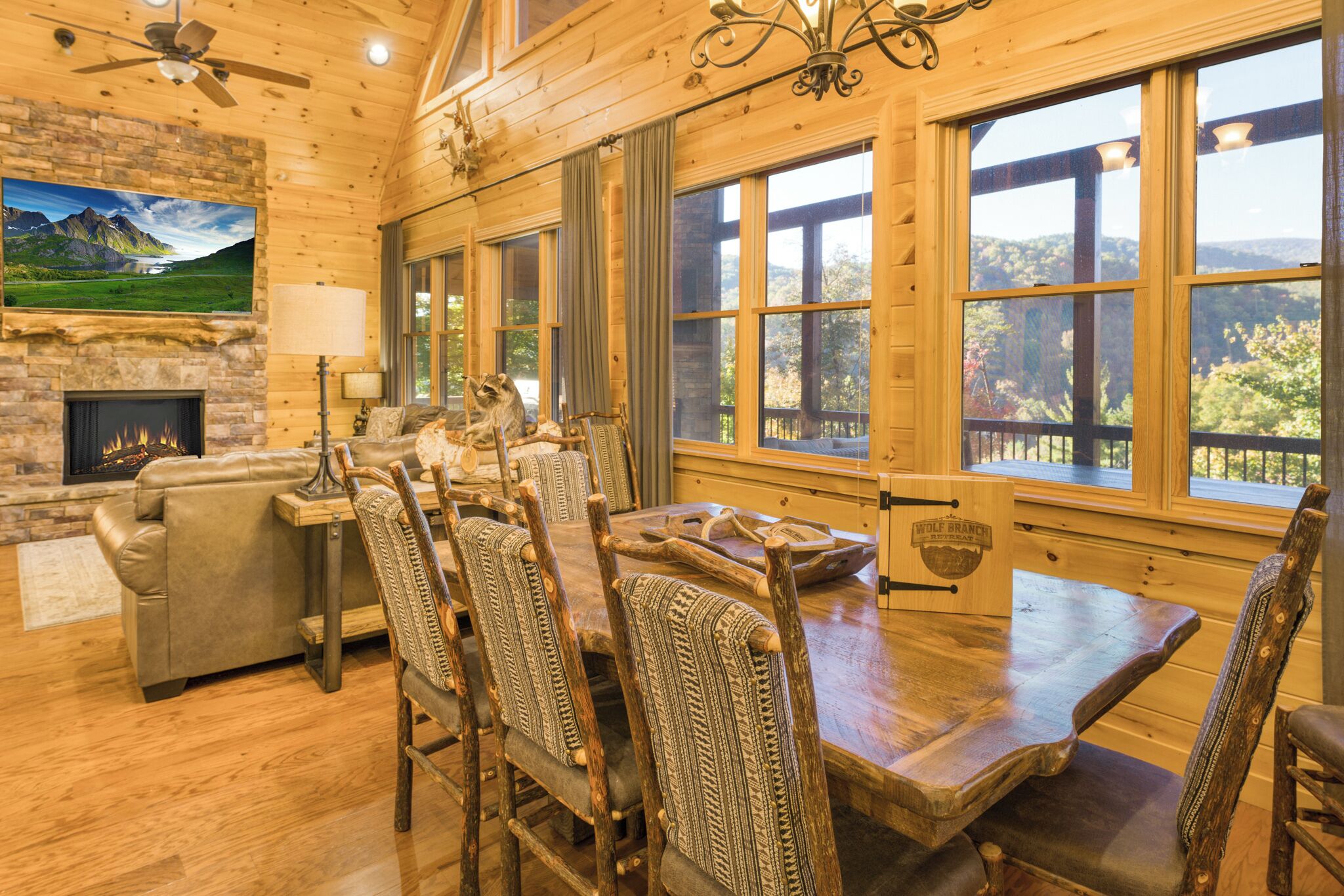 A rustic wooden interior with a fireplace, dining table, and chairs, large windows with a view of the outdoors.