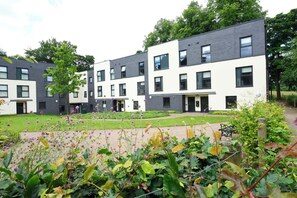 A modern building with multiple floors, large windows, and a well-maintained garden area. - Alexander Court Townhouses (Stirling)
