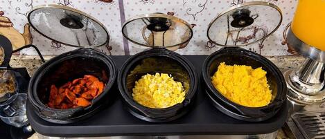A kitchen with three slow cookers on a stove, each containing different food items.