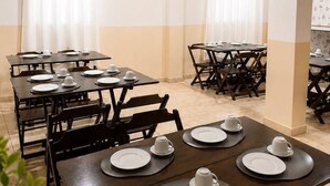 A dining area with multiple tables set for service, featuring white plates and cups, and wooden chairs. - NOSSO HOTEL (Três Lagoas)