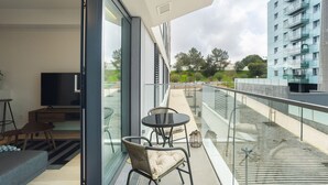 A modern balcony with a glass railing, a sofa, a TV, and a dining area. - Modern Lisbon W Balcony by Homing (Lisbon)
