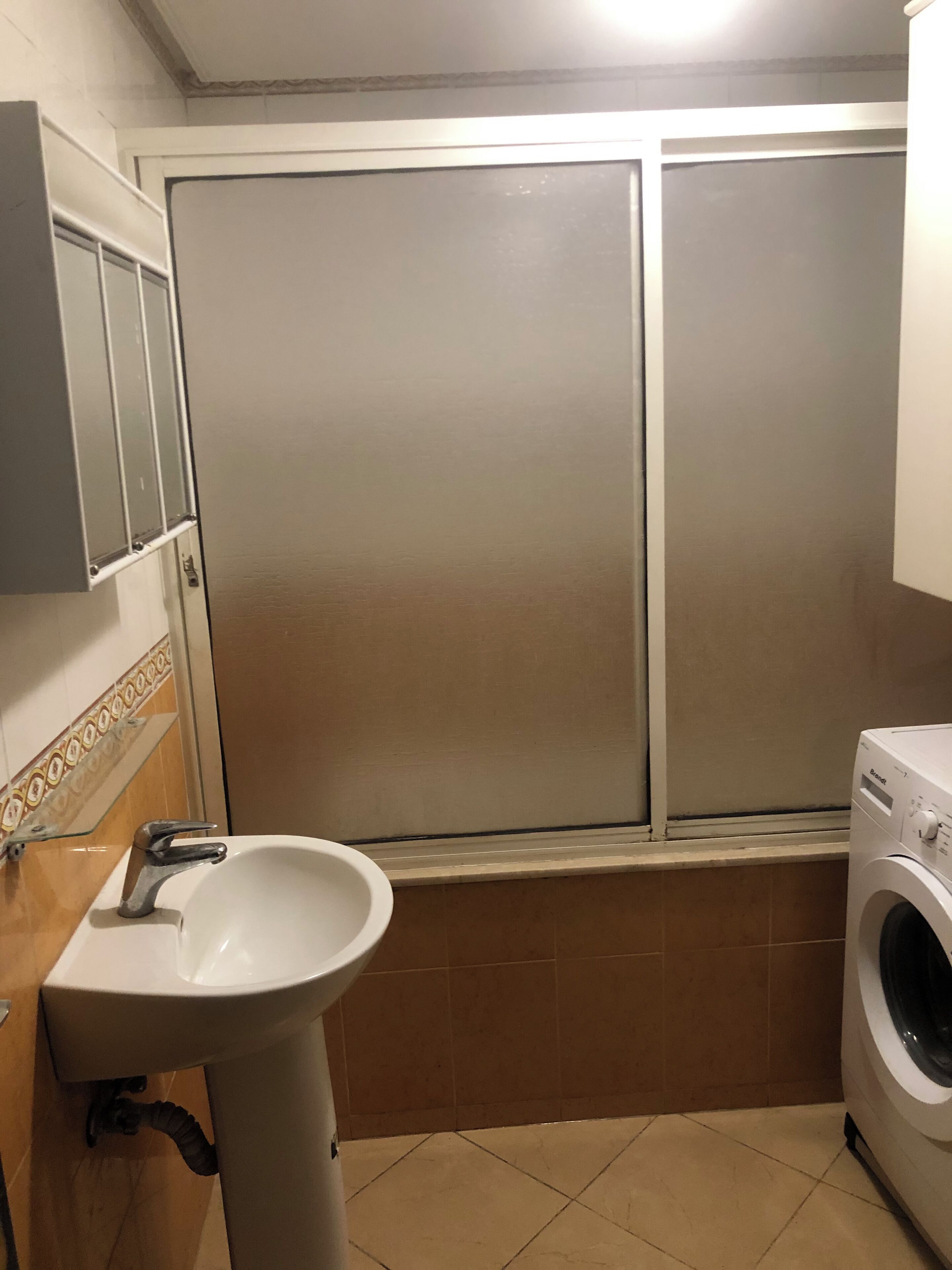 A compact bathroom with a sink, a washing machine, and a sliding door.