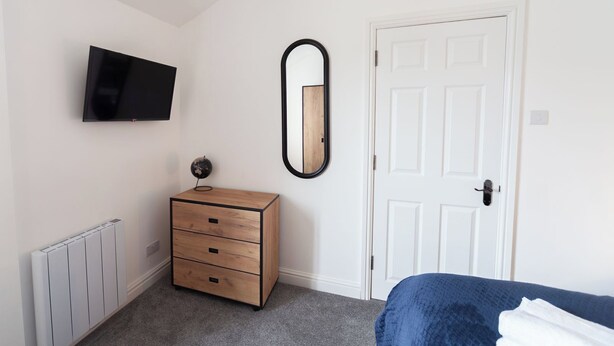 Ein Schlafzimmer mit einem Bett, einem Schminktisch, einem an der Wand montierten Fernseher, einer Tür und einer Heizung.