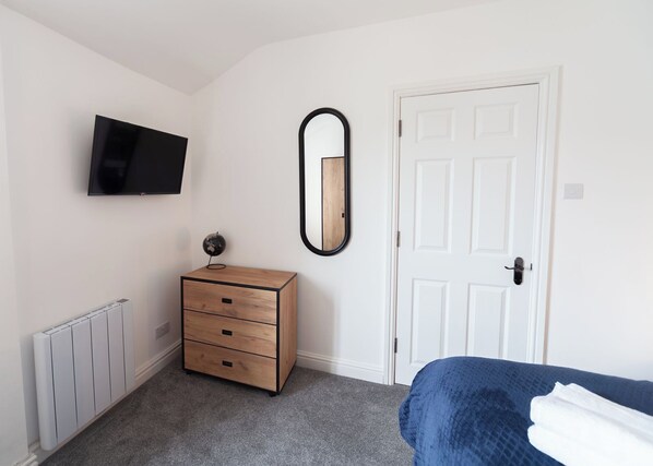 Un dormitorio con cama, cómoda, televisor montado en la pared, puerta y radiador.
